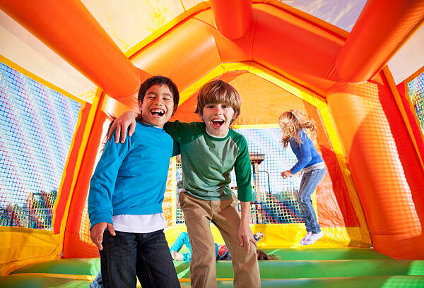 Multi-ethnic boys laughing in bouncy castle, girls jumping in background.